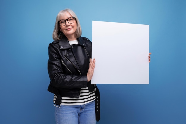 Confident mature business woman with gray hair demonstrates whatman paper with a mockup on a bright