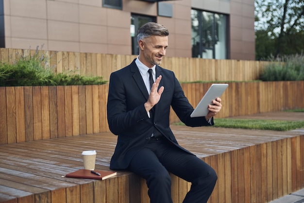 Confident mature businessman using digital tablet while sitting outdoors near office building