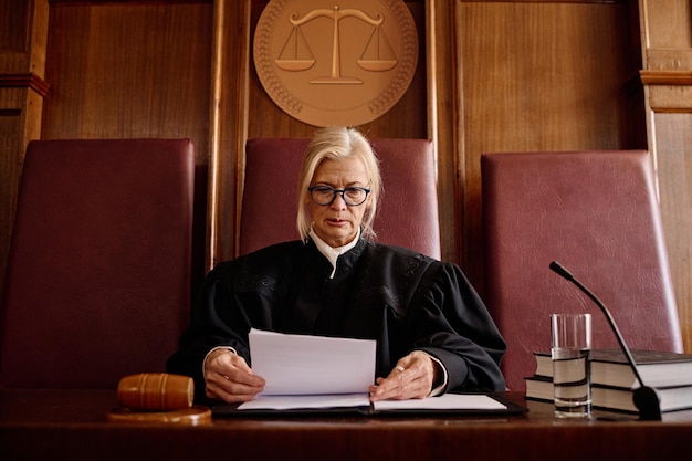 Confident mature female judge in black mantle looking through documents