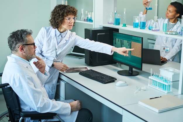 Confident mature female virologist pointing at computer screen