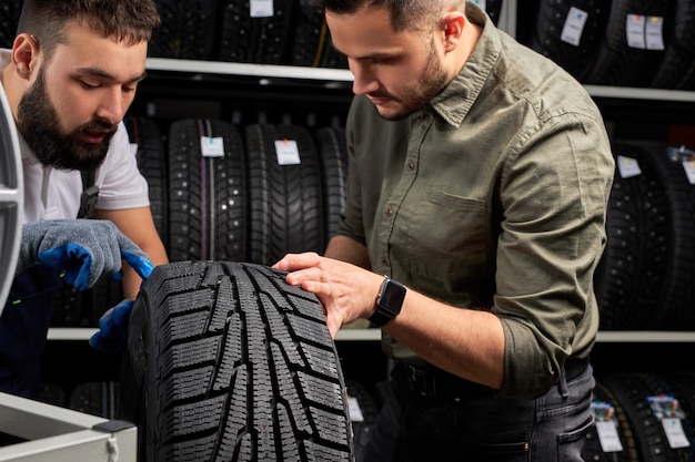 Confident mechanic and client checking tires in store, having conversation in shop, customer is going to make purchase. soft focus