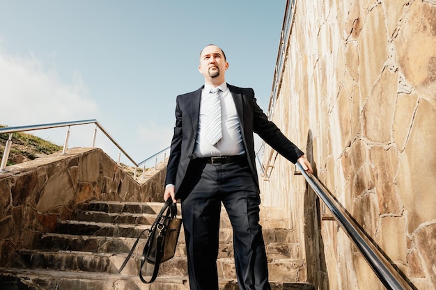 青を身に着けているビジネスマンの2階のクローズアップを歩いているブリーフケースを持つ自信を持って中年のビジネスマン