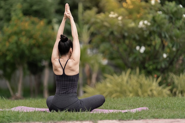 A confident middle-aged Asian woman in sports outfit doing yoga exercise on the yoga mat outdoor in the backyard in the morning. Young woman doing yoga exercise outdoor in the nature public park