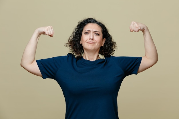 Confident middleaged woman wearing tshirt looking at camera making strong gesture isolated on olive green background