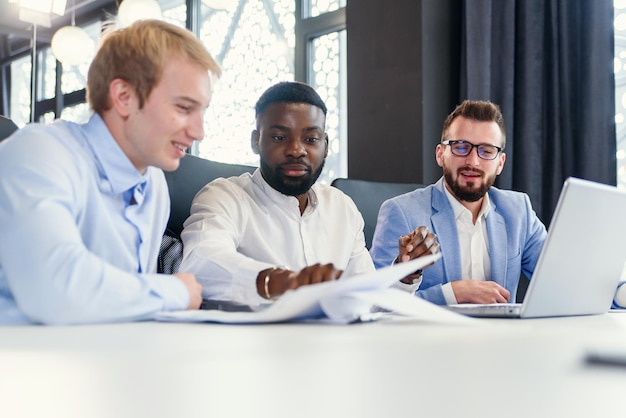 Photo confident mixed races businessmen sitting at the office table and using computer to revision their