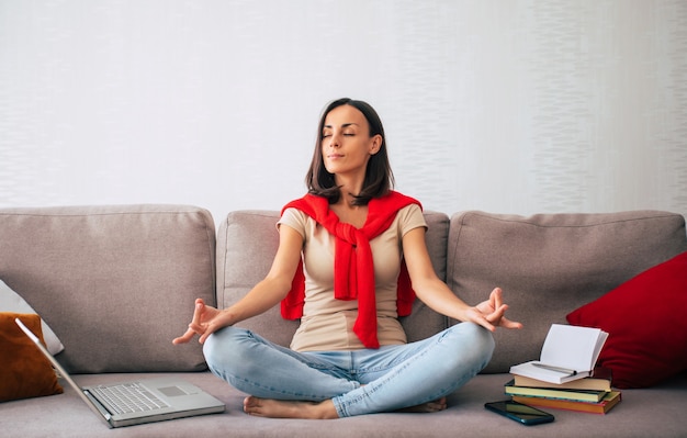 Confident modern cute young woman is online working and relaxing at home on the couch with her laptop on the freelance job