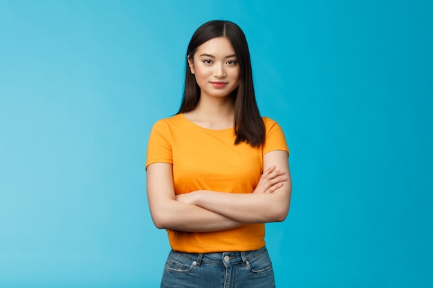 Confident motivated feminine asian woman feel empowered deal office problems manage business, hold hands crossed chest, smiling determined, wear yellow t-shirt, stand blue background