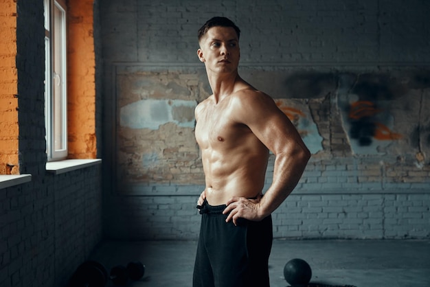 Photo confident muscular man holding hands on hip while standing in gym