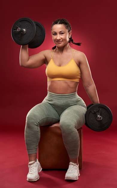 Confident plus size young woman in fitness attire exercising on\
gray background