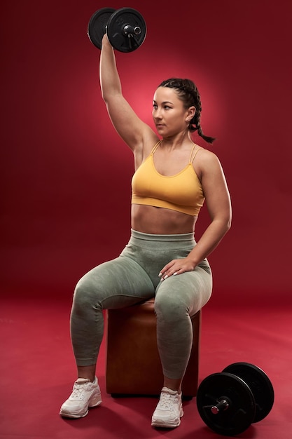 Confident plus size young woman in fitness attire exercising on\
gray background