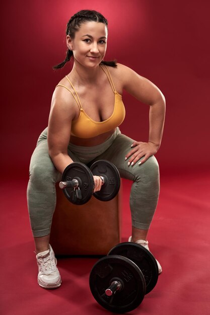 Confident plus size young woman in fitness attire exercising on\
gray background