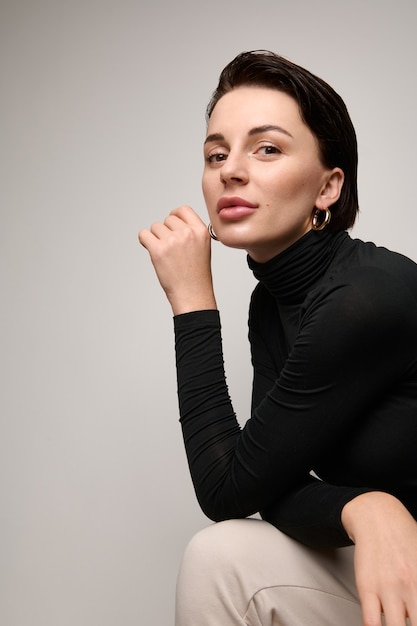 Confident portrait of beautiful fashionable attractive brunette European woman sitting three quarters to white background with copy space.