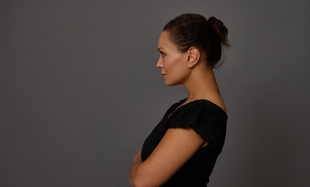 Photo confident portrait of middle aged woman dressed in black standing side to a gray wall background with copy space for advertisement