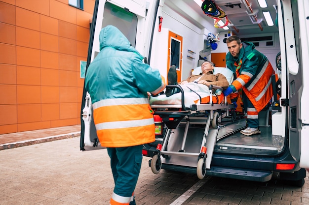 Foto medici fiduciosi e professionali che scaricano un paziente malato da un'ambulanza su una barella vicino all'edificio dell'ospedale