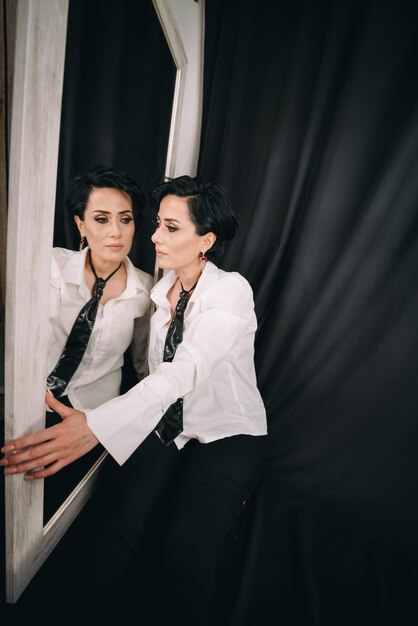 Confident radiant woman in white shirt posing with a mirror and examining her reflection