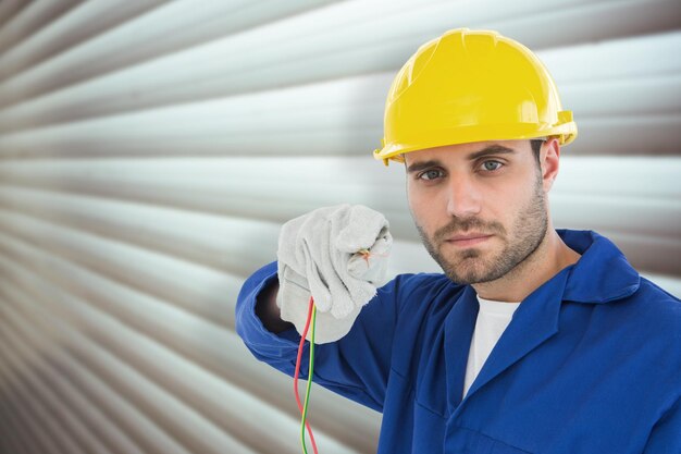 Confident repairman holding cables against grey shutters