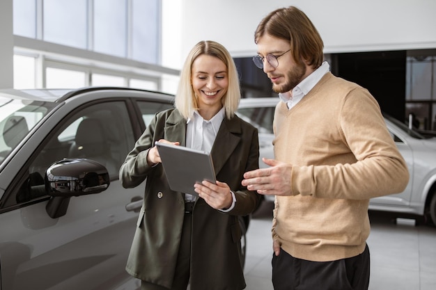 Photo confident saleswoman explaining all car features using tablet to handsome owner