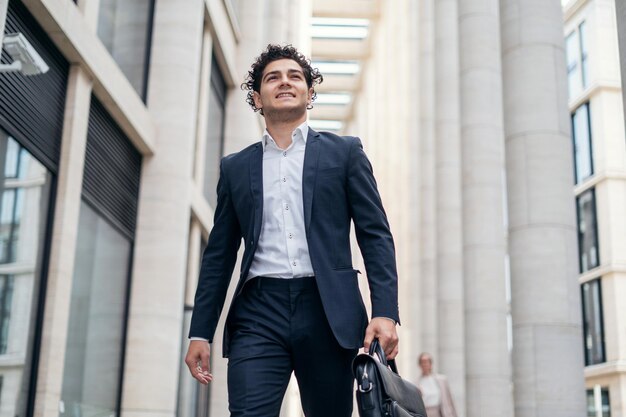 A confident satisfied male manager in an official suit goes to the office and holds a briefcase