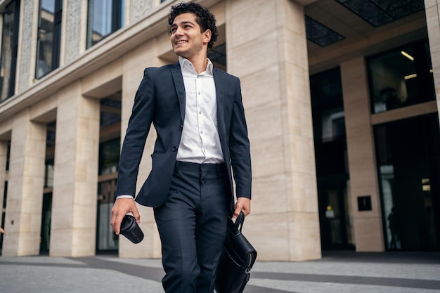 A confident satisfied male manager in an official suit goes to the office and holds