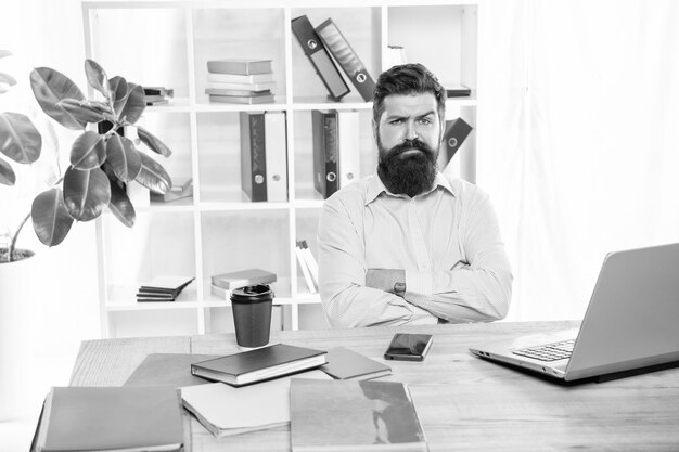 Confident sceptical businessman keeping arms crossed sitting at office desk confidence