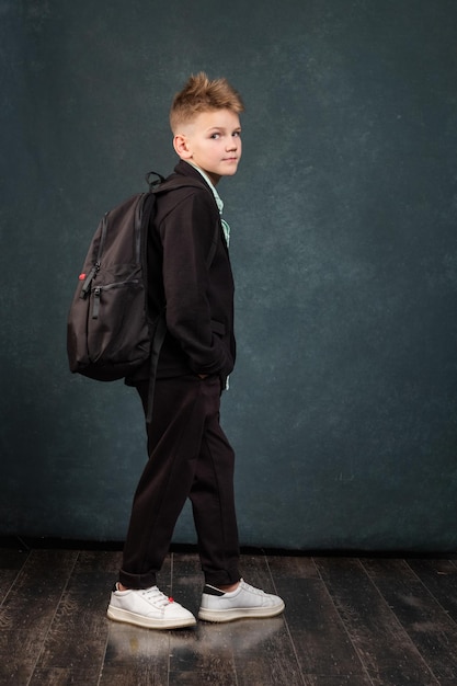 Confident schoolboy with backpack on black background