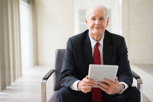 confident senior Caucasian manager sitting in armchair with digital tablet 