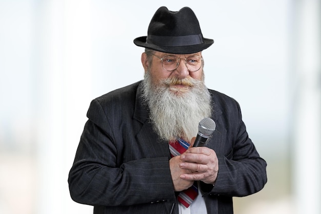 Фото Уверенный старший мужчина с бородой держит микрофон на размытом фоне. концепция публичного выступления.