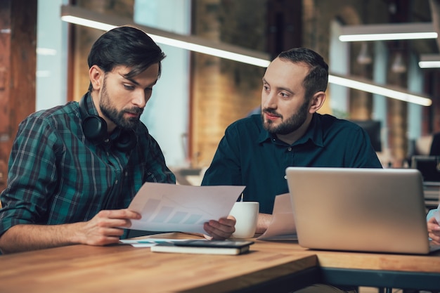 Confident serious coworkers sitting at the table with a graphic chart and sharing their ideas