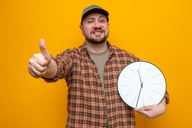 Confident slavic cleaner man holding clock and thumbing up