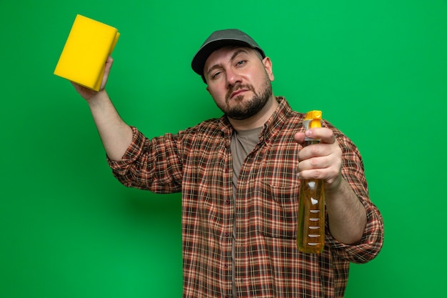 Confident slavic cleaner man holding sponge and spray cleaner