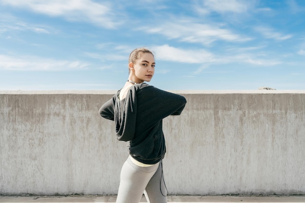 Foto la ragazza snella sicura si riscalda prima dell'allenamento all'aria aperta, conduce uno stile di vita attivo