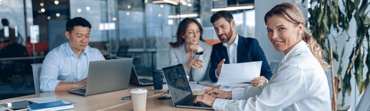 Confident smiling businesswoman sitting at the office with group of colleagues on background