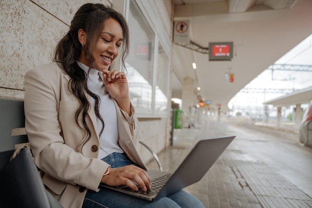 Уверенная улыбающаяся деловая женщина с помощью портативного компьютера во время видеозвонка сидит на скамейке