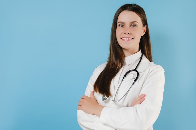 Fiduciosa dottoressa sorridente indossa camice bianco medico, stetoscopio guarda la telecamera in piedi su sfondo blu. ritratto di giovane donna medico professionista medico medico