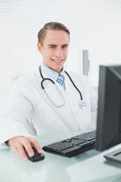 Confident smiling male doctor with computer at medical office