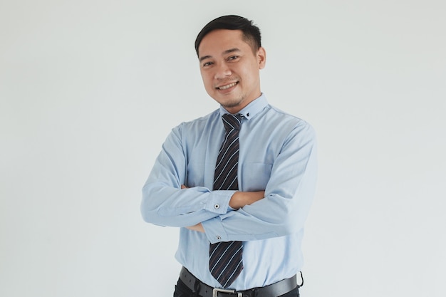 Confident smiling sales man wearing blue shirt and tie posing with arms folded on white background