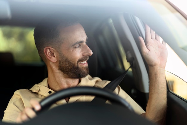 Confident smiling taxi driver waving hand waiting for client sitting in car. Transportation concept