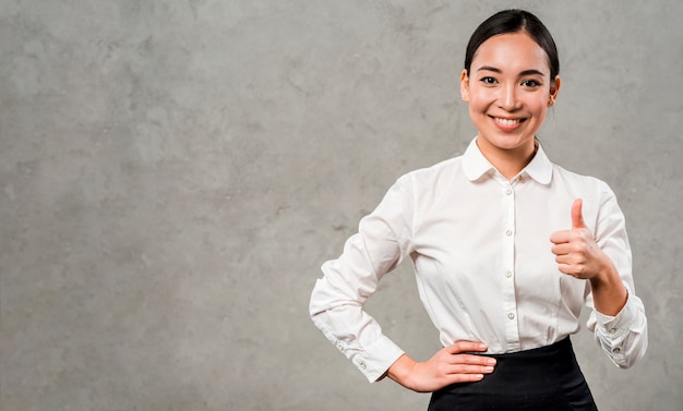 Photo confident smiling young businesswoman showing thumb up sign standing against grey wall