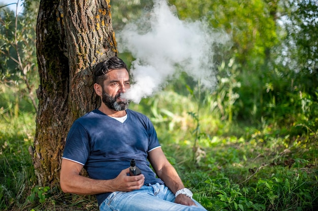 Confident smoker blowing a lot of smoke using vape electronic smoke device. Modern ways of quitting tobacco.