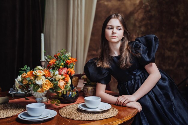 Confident spanish girl in black dress with long dark hair standing at table with flowers candle