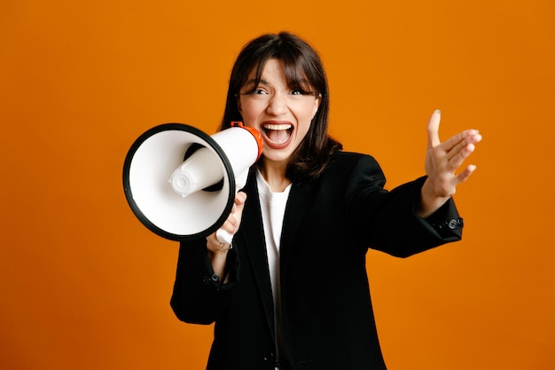 Confident speaks on loudspeaker young beautiful female wearing black jacket isolated on orange background