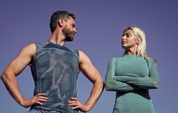 Уверенный спортивный мужчина и женщина в спортивной одежде расслабляются на фоне неба
