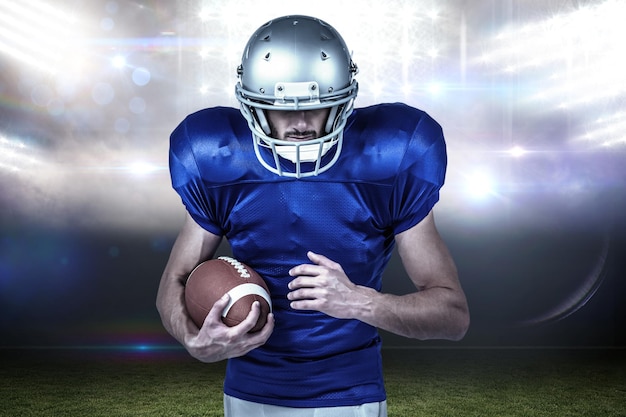 Confident sports player holding ball against sports pitch