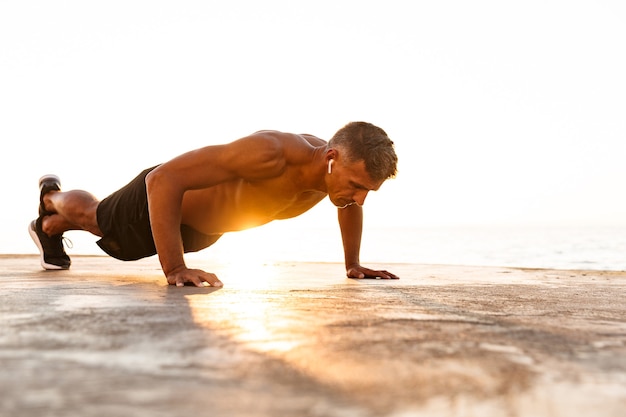 Confident sportsman doing push-ups at the beach