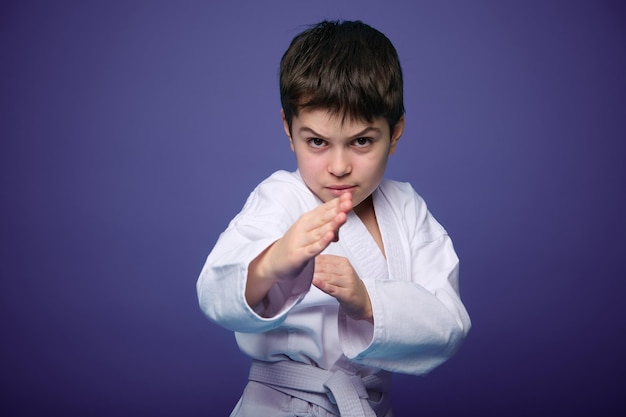 Confident strong kid aikido fighter practicing martial skills on purple background with advertising copy space Oriental martial arts practice concept