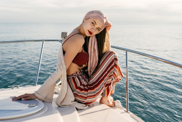 Confident stylish girl in summer clothes sits on a ship and looks at the camera, sails on the Caribbean sea