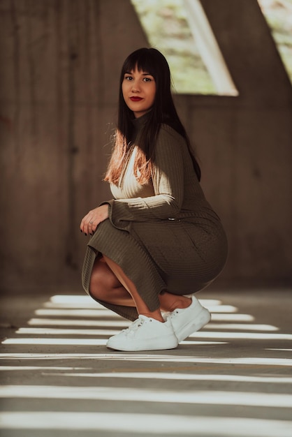 A confident and stylish plussize woman posing by a modern building in an olive green dress radiating