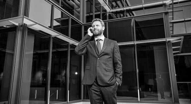 Уверенный успешный бородатый бизнесмен в официальном костюме, говорящий по смартфону о современной коммуникации