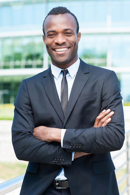 Confident and successful businessman. Handsome young African man in full suit keeping arms crossed and looking at camera while standing outdoors