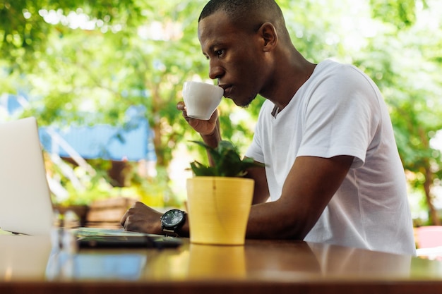 Confident and successful multiracial businessman drinking coffee and work chatting online using laptop in street cafe